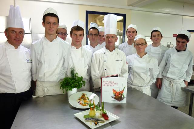 Gérard Bosher à gauche et Jean-Yves Le Moigne professeur de cuisine du lycée avec les élèves , avec le nouvel ouvrage de Gérard Bosher et le plat réalisé par les futurs cuiniers.
