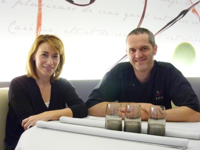 Maryline et Eric Girardin attablés avec derrière eux la toile qui est une partie de leur signature